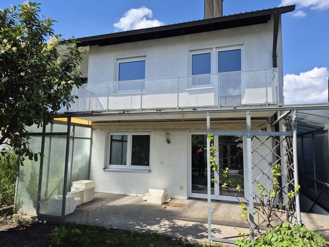 Weiße Fenster und Terrassentür an Hausrückseite mit Balkon und überdachter Terrasse