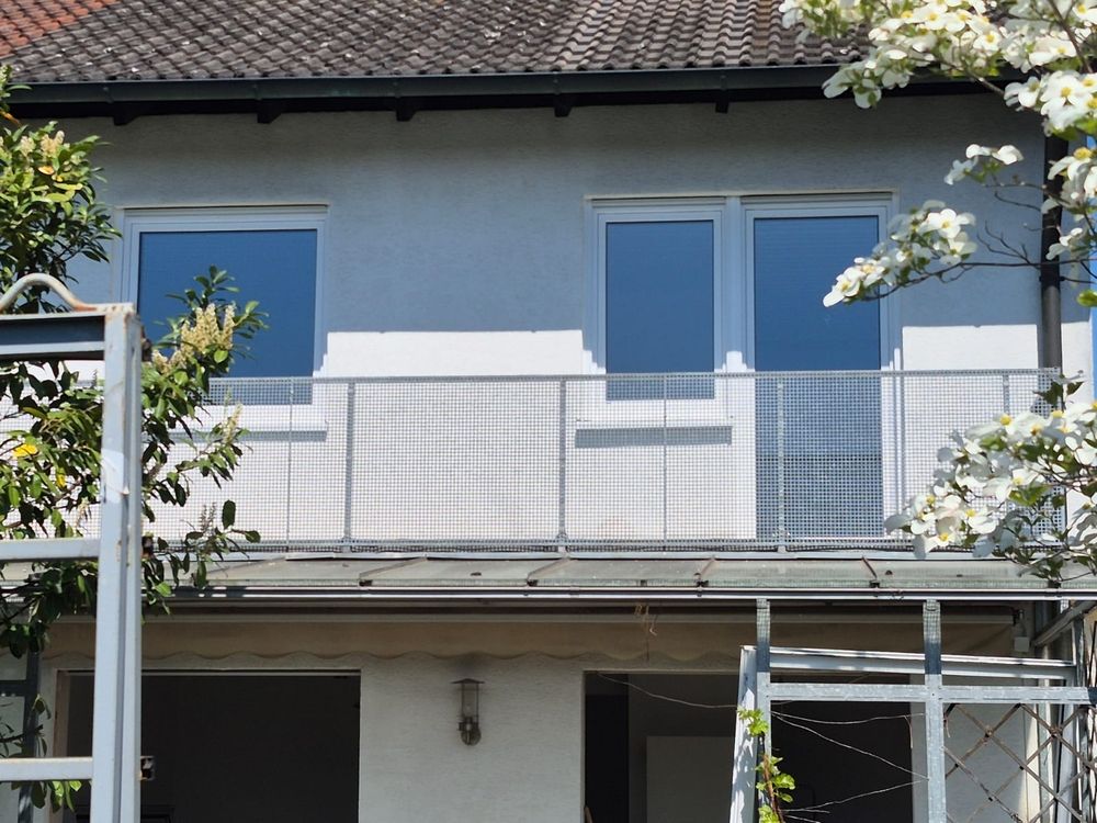 Drei neu eingebaute Kunststofffenster an Hausfassade hinter Balkon mit Gitterzaun