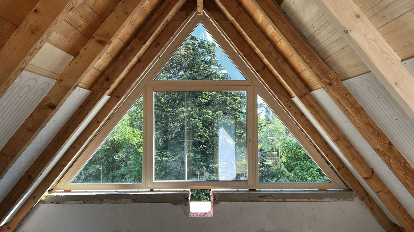 Dreieckiges Sonderformat-Fenster im Giebel eines Dachgeschoss-Rohbaus mit Blick ins Grüne